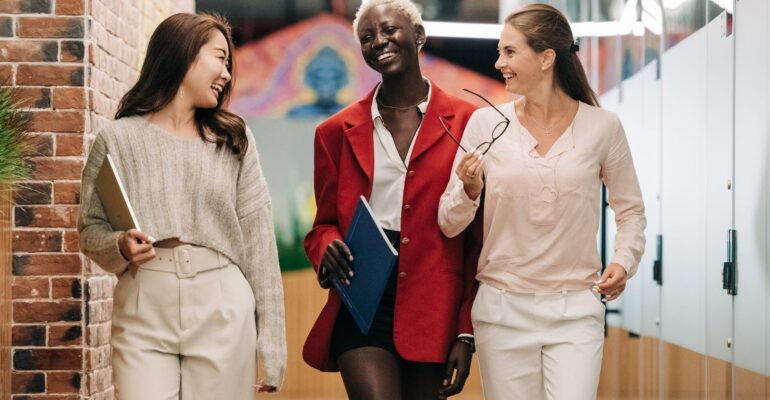 diverse successful businesswomen smiling and walking together in modern workplace