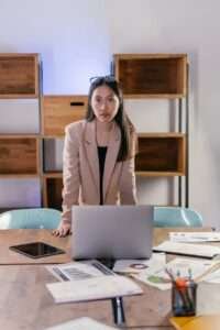 woman in a beige blazer standing near a laptop